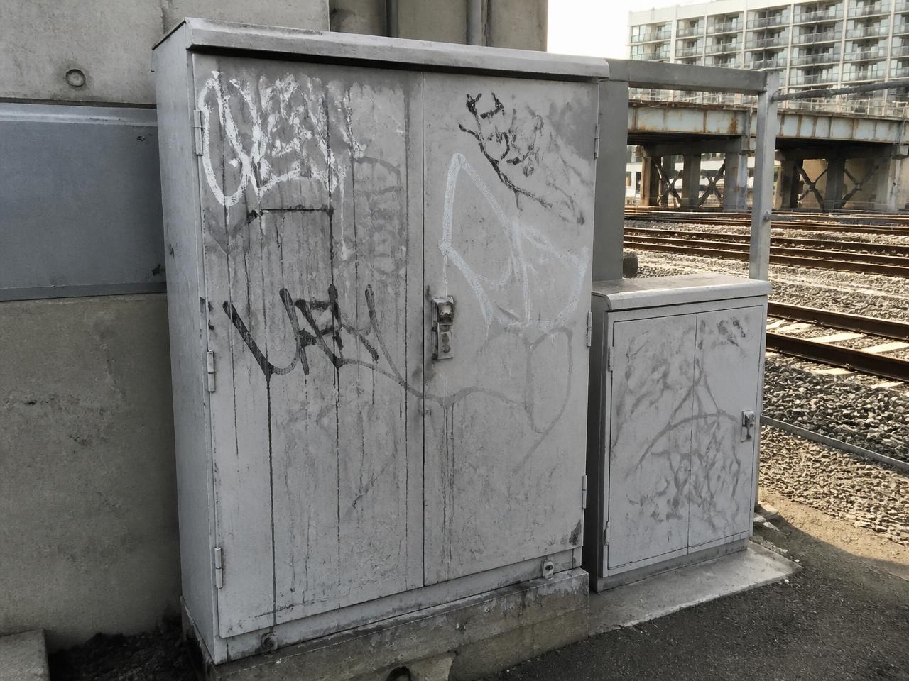 Weathered utility boxes with indistinct graffiti near transportation infrastructure